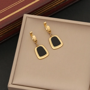 Detailed close-up of golden geometric earrings with black trapezoid enamel pendants