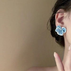 Elegant iris blue flower stud earrings with gold trim worn by a model in soft lighting