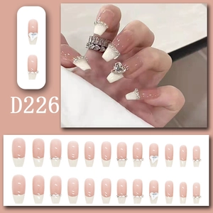 Macro detail of long French press-on nails with nude pink base, white tips, and rhinestones