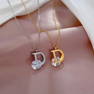 Detail of silver and gold D-letter necklaces with round zircon on silk fabric