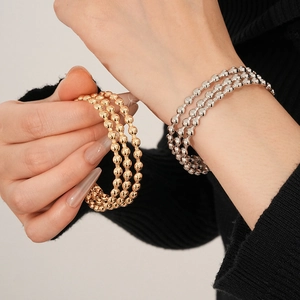 Dettaglio di bracciali a sfere multistrato oro e argento con finitura metallica lucida