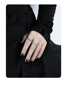 Detail of hollow silver mesh ring and green enamel ring on hand with black aesthetic