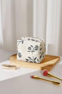 Macro detail of floral embroidery on off-white linen cosmetics bag with gold zipper ring