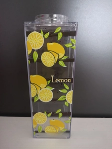 Close-up detail of transparent square water bottle with vibrant lemon print and green leaves