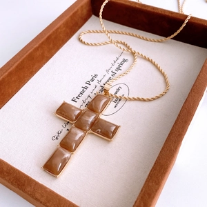 Macro detail of gold twisted chain and resin inlaid cross pendant on a jewelry tray