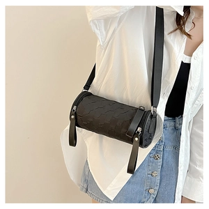 Detail of black cylinder crossbody bag with quilted texture and wide strap on model