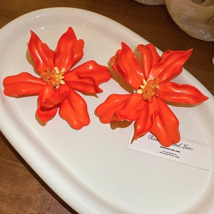 Close-up of oversized red acrylic flower earrings with yellow beaded centers on white tray
