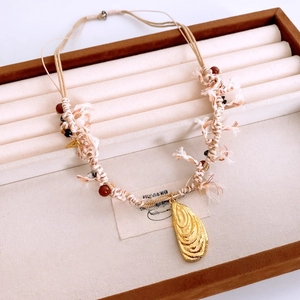 Detail of bohemian woven cord necklace with a golden mussel shell pendant on a display tray