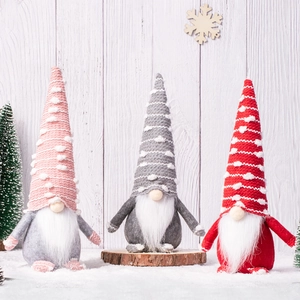 Three plush Christmas gnomes with knitted hats and white beards on a snowy wood background