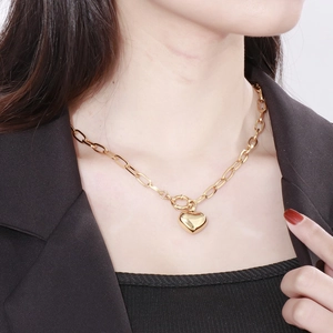 Close-up of a gold heart pendant on a chunky chain necklace worn on a model's neck