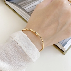 Detailed view of an irregular 18K gold-plated silver bangle on a minimalist model sleeve