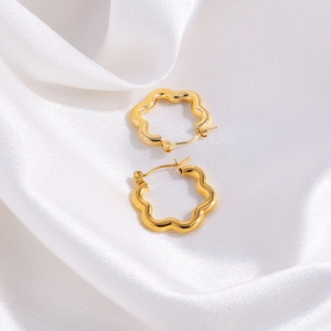 Detailed view of gold flower-shaped stainless steel earrings on white silk fabric