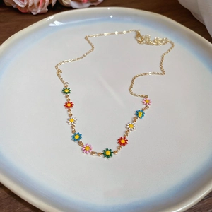 Close-up of golden necklace with colorful enamel daisy pendants on a ceramic tray
