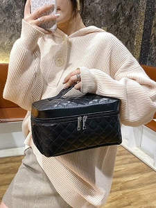 Black quilted PU leather travel makeup bag with double zippers and handle held by model
