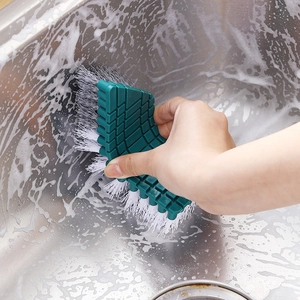 Flexible dark green cleaning brush with white bristles scrubbing a stainless steel sink
