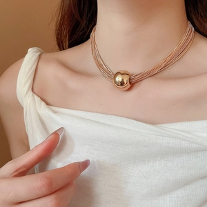 Detailed view of layered gold snake chain necklace with large round metal pendant on neck