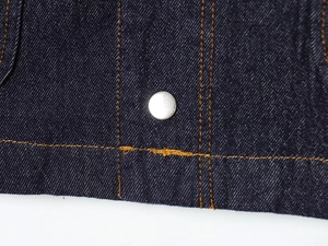 Detailed macro view of dark blue denim fabric with orange stitching and silver rivet detail