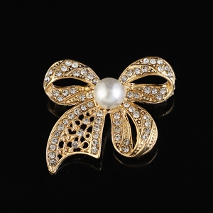 Détail d'une broche nœud dorée ornée de strass et d'une perle centrale nacrée