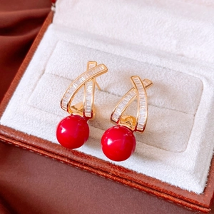 Detail of 18k gold plated stud earrings with sparkling white zircons and red round beads