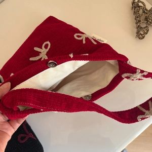 Détail macro du cabas en velours côtelé rouge avec bouton pression et broderie nœud blanc