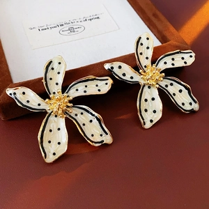 Close-up of vintage flower earrings with black polka dots on a cream velvet background