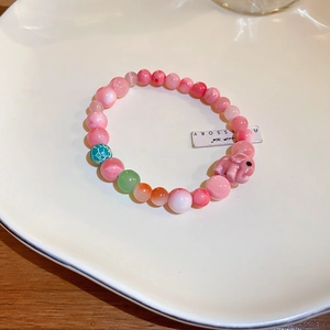 Detail of beaded bracelet with pink beads and a cute pink elephant pendant on a white plate