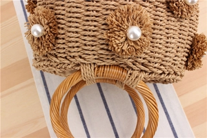 Detail of straw bucket bag featuring woven raffia flowers and center pearl accents