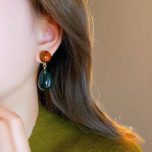 Detail of amber bead and dark green resin water drop pendant earring on a female model