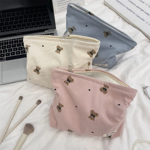 Detailed view of three corduroy teddy bear makeup bags with silver zippers in a cozy setting
