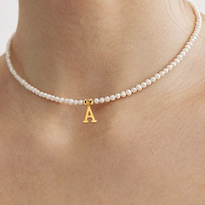 Close-up of pearl necklace with a gold letter A pendant worn on a model's neck