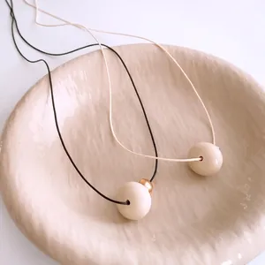 Ethnic wax rope necklaces with minimalist cream resin sphere pendants on ceramic tray