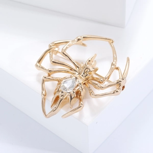 Detail of a golden spider brooch featuring a clear teardrop gemstone inlay on a white base