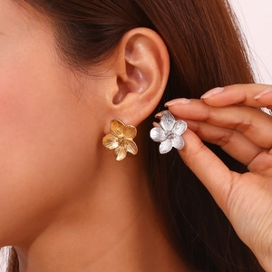 Gold and silver 3D floral earrings with brushed texture on female model close-up