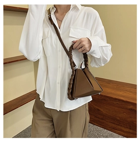 Detail of dark brown geometric handbag featuring a braided handle and metal feet