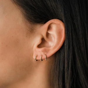 Three minimalist 925 sterling silver golden huggie hoop earrings worn in a stacked style