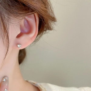 Close-up of a delicate heart-shaped zircon stud earring worn on a model ear