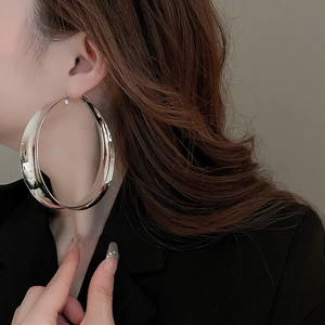 Close-up of oversized polished silver hoop earring on model with metallic finish
