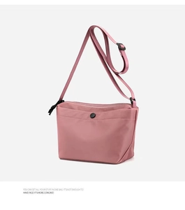 Detailed macro shot of a light pink nylon crossbody bag with black snap button detail