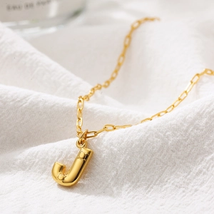 Detailed macro view of a golden bubble letter J pendant with textured dot relief on a chain