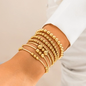 Close-up of a stacked gold beaded bracelet set with heart charms on a model wrist