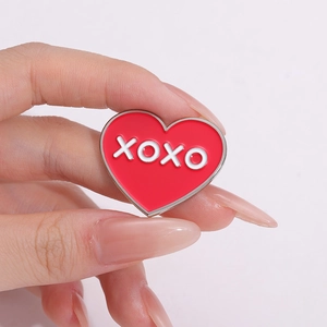 Broche cœur rouge émaillé avec texte XOXO tenue à la main sur fond rose doux