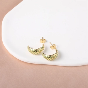 Detail of C-shaped gold earrings with green enamel stripes on a white display tray