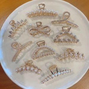 Flat lay of gold hair claws with faux pearls and rhinestones on white ceramic plate
