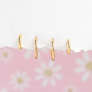 Detailed view of four 18K gold-plated smooth hoop earrings in various sizes on white paper