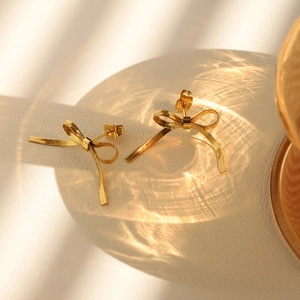 Macro shot of gold bow stud earrings with polished metallic texture on leather background