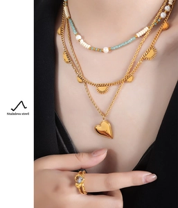 Detail of layered stainless steel gold necklaces with heart pendant and pearl beads