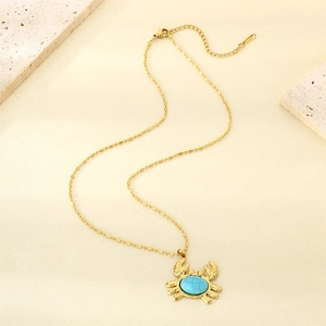 Macro shot of gold crab pendant featuring blue natural stone on warm beige stone background