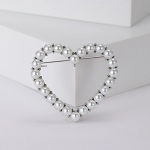 Elegant silver hollow heart brooch with white pearls and rhinestones on a white pedestal
