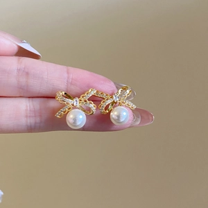 Detail shot of 18k gold plated bow stud earrings featuring sparkling zircons and a round pearl