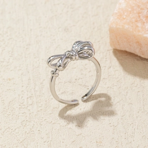 Macro shot of silver bow ring with adjustable band on textured beige background
